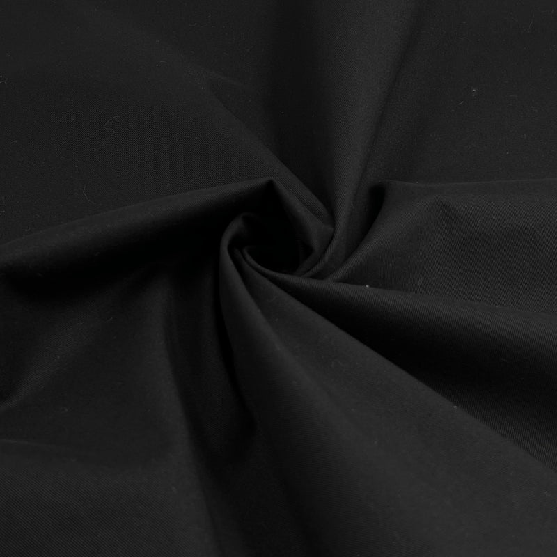 Closeup of black cotton/lycra stretch twill fabric folded into a swirl. This material displays 20% stretch widthwise, and is ideal for fitted suits, jackets, trousers, and more. 