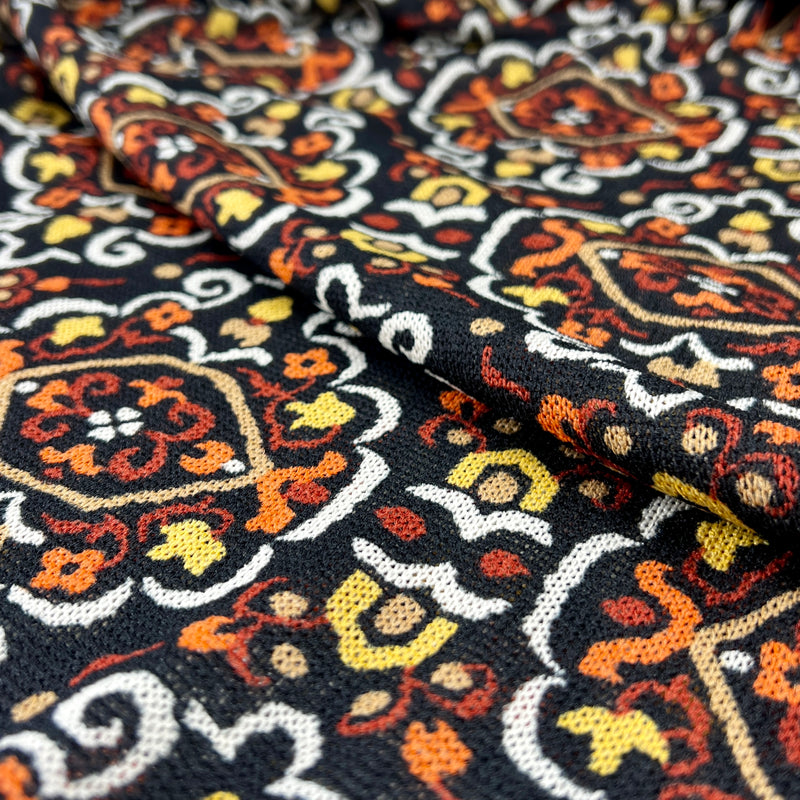 Close-up of patterned fabric with intricate designs in orange, yellow, and white on a black background.