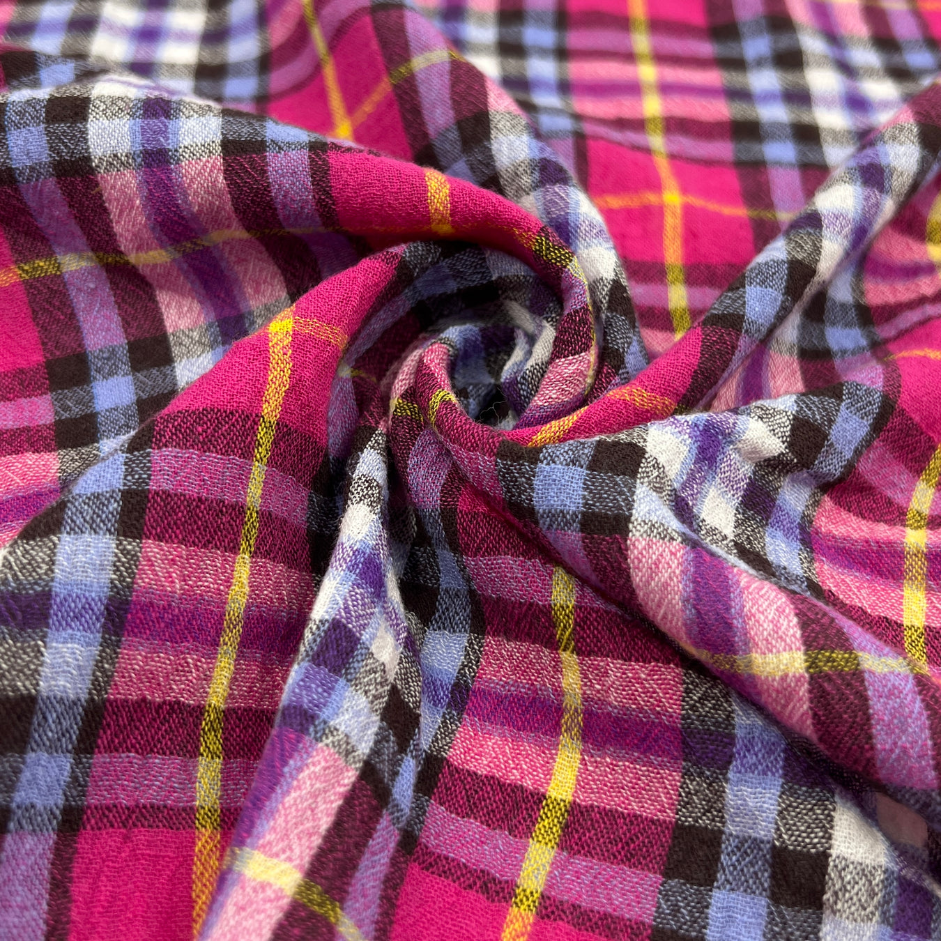 Close-up of plaid fabric with pink, purple, and yellow colors pulled into a swirl to show off lightweight body and drape.