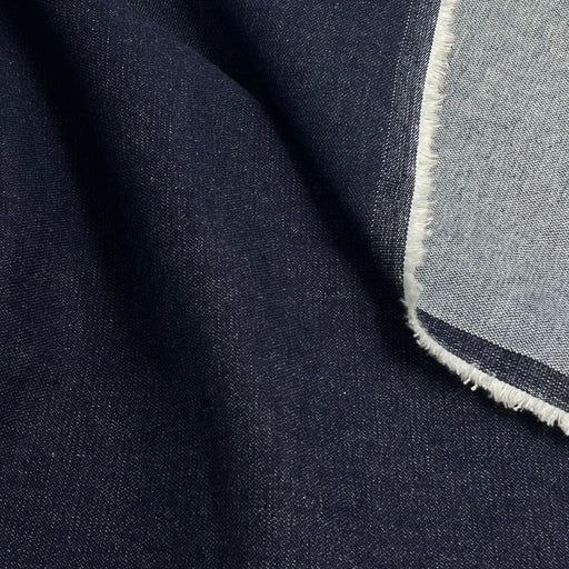 Close-up of a folded dark navy fabric with a lighter gray-blue reverse side and frayed edge.