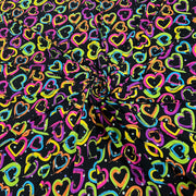 Black fabric with a vibrant, multicolored heart pattern, arranged in a spiral drape to show its texture and print.