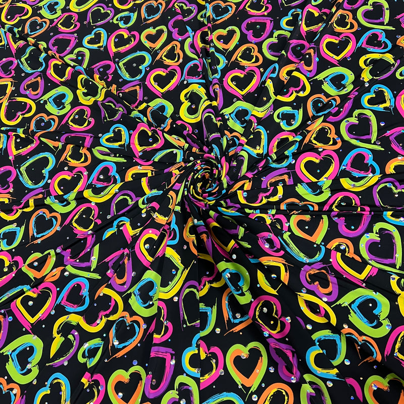 Black fabric with a vibrant, multicolored heart pattern, arranged in a spiral drape to show its texture and print.