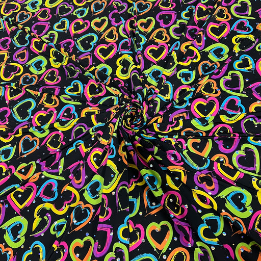 Black fabric with a vibrant, multicolored heart pattern, arranged in a spiral drape to show its texture and print.