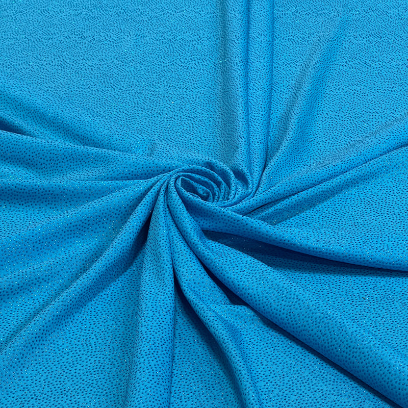 A close-up of bright blue textured fabric arranged in a spiral drape, showing the material's fine dotted pattern and folds.