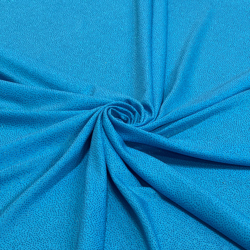 A close-up of bright blue textured fabric arranged in a spiral drape, showing the material's fine dotted pattern and folds.
