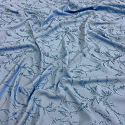 Light blue fabric with an allover embroidered floral vine pattern in darker blue and silver sequins, draped to show texture and sheen.