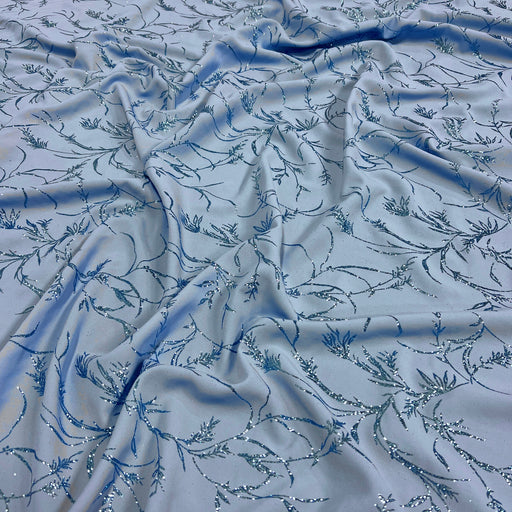 Light blue fabric with an allover embroidered floral vine pattern in darker blue and silver sequins, draped to show texture and sheen.