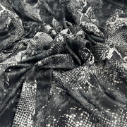 Black and white snakeskin print fabric draped in soft folds, showing a glossy texture with a scale pattern.