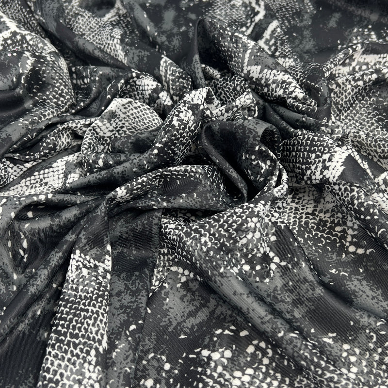 Black and white snakeskin print fabric draped in soft folds, showing a glossy texture with a scale pattern.