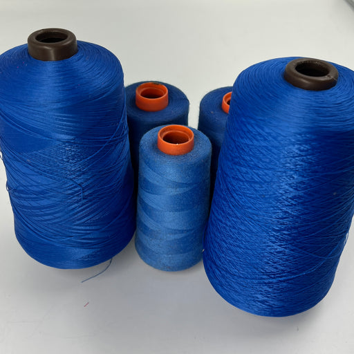 Several large cones of blue thread or yarn with dark brown and orange inner cores, arranged on a plain white surface.