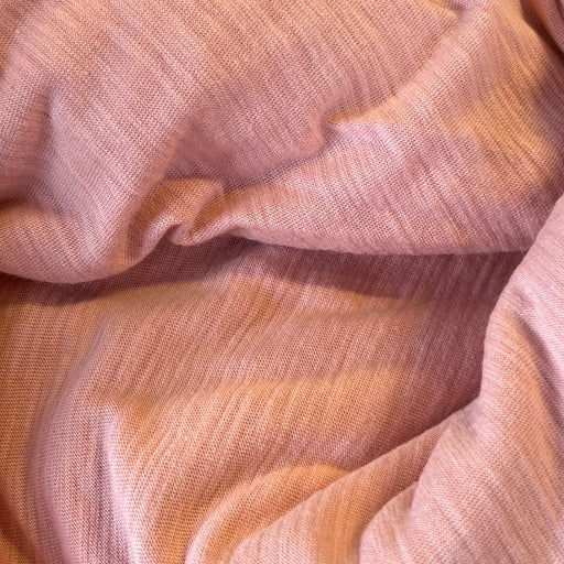 A close-up of draped dusty pink fabric with a soft, textured weave.