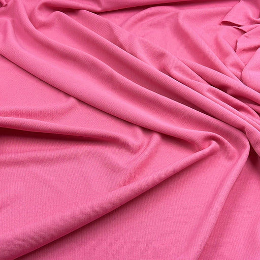 A close-up of draped pink fabric with soft folds and a smooth texture filling the frame.
