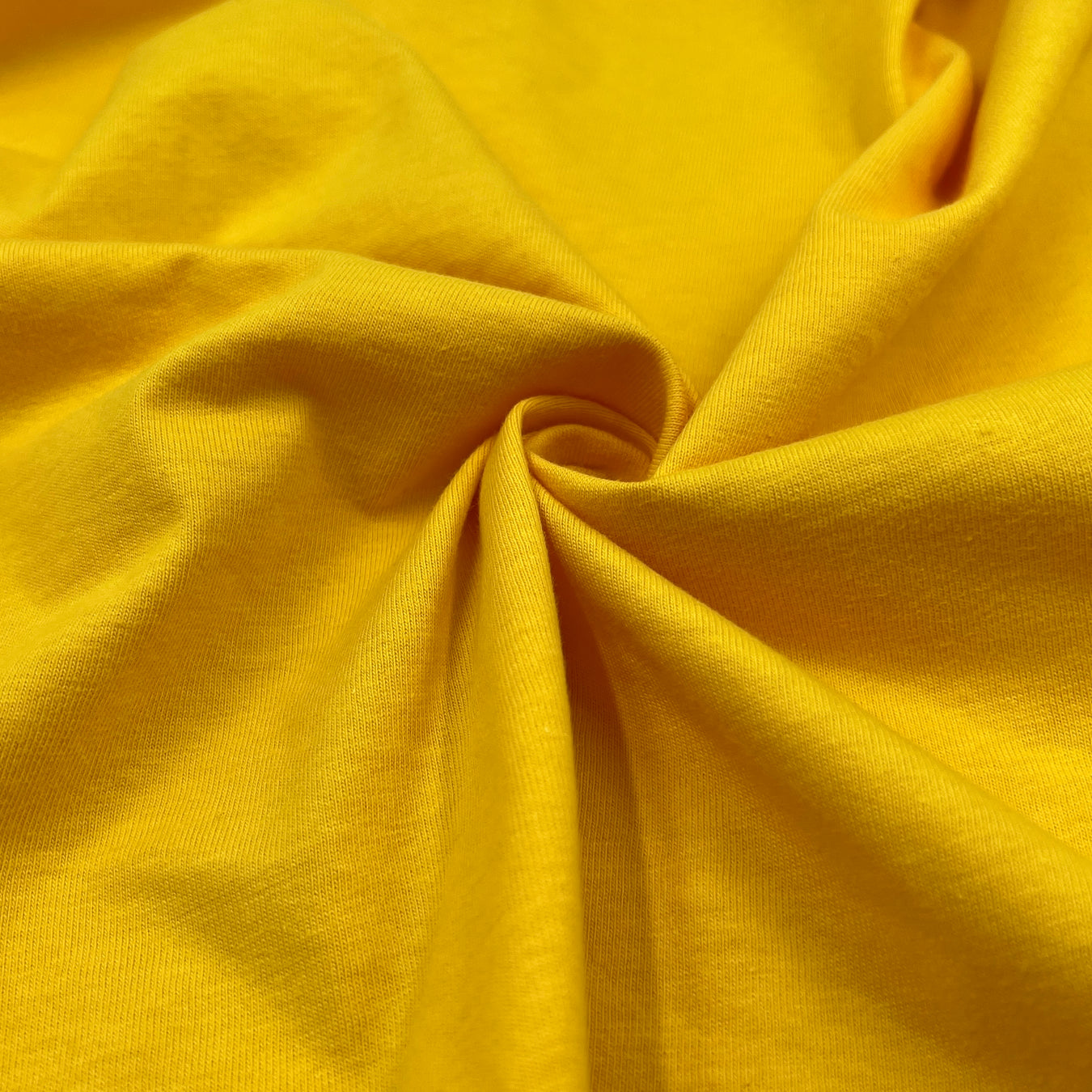 Closeup of 100% cotton jersey in vibrant yellow color pulled into a swirl. 