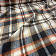 A close-up of draped plaid fabric with a warm-toned pattern featuring navy, charcoal, beige, and rust orange stripes on an off-white base.