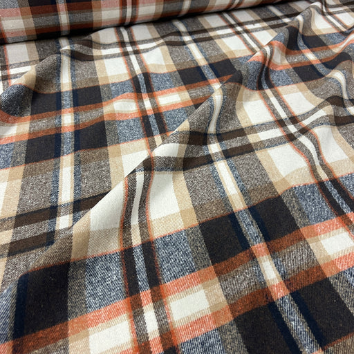 A close-up of draped plaid fabric with a warm-toned pattern featuring navy, charcoal, beige, and rust orange stripes on an off-white base.