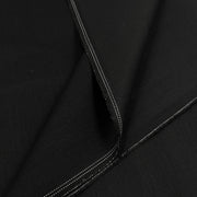 A close-up of black fabric with visible diagonal twill texture and double white stitched edges.