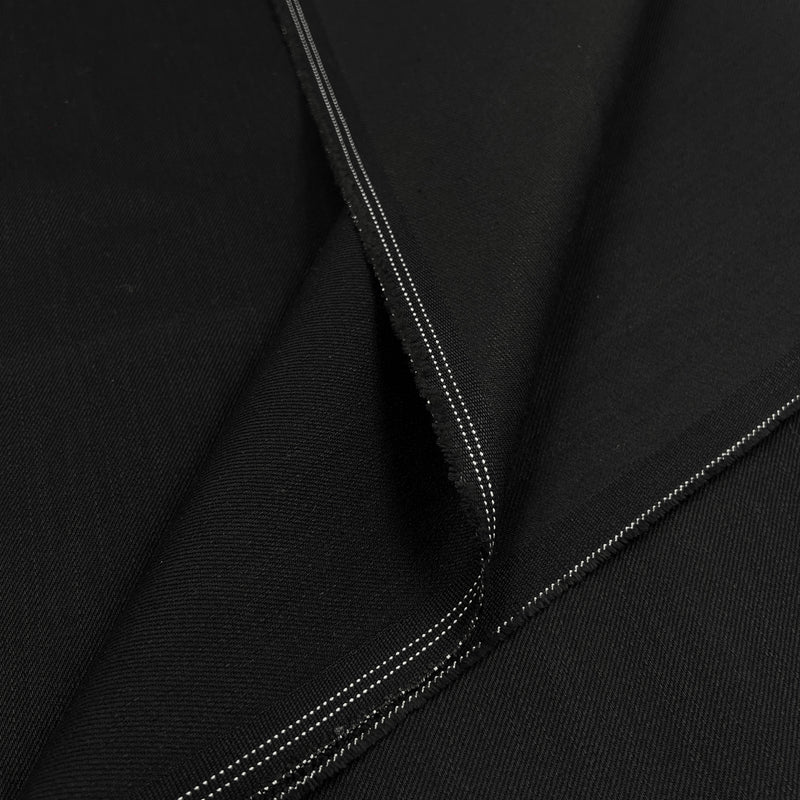 A close-up of black fabric with visible diagonal twill texture and double white stitched edges.