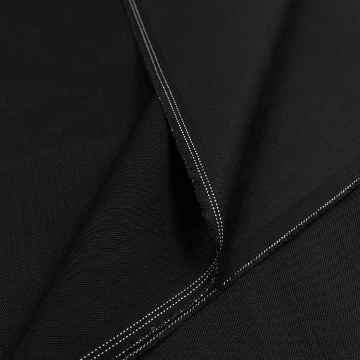A close-up of black fabric with visible diagonal twill texture and double white stitched edges.
