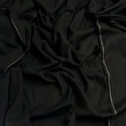 A close-up of draped black fabric with visible woven texture and a narrow gray stitched edge running vertically.