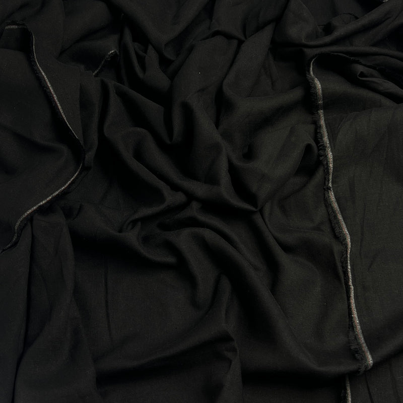 A close-up of draped black fabric with visible woven texture and a narrow gray stitched edge running vertically.