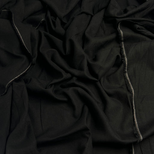 A close-up of draped black fabric with visible woven texture and a narrow gray stitched edge running vertically.