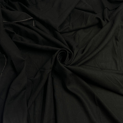 Black fabric draped in soft folds, showing a smooth matte texture with a gathered swirl in the center.