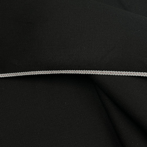 A close-up of black fabric with a thin, braided silver cord or trim running horizontally across the center.