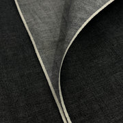 Closeup of lightweight black yarn dye selvedge denim fabric showing off both sides of selvedge. 