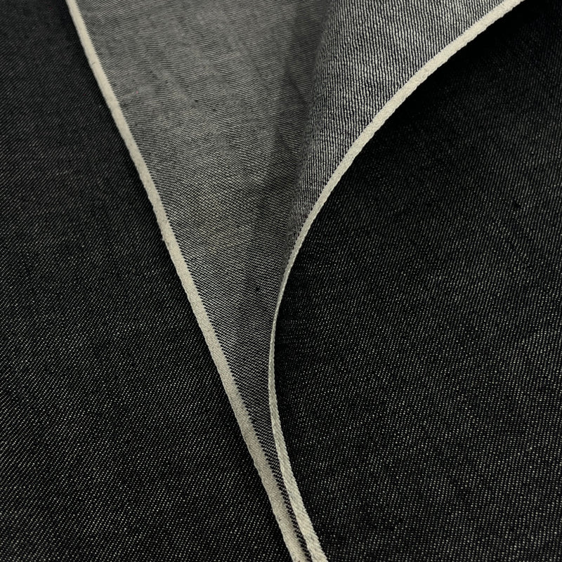 Closeup of lightweight black yarn dye selvedge denim fabric showing off both sides of selvedge. 