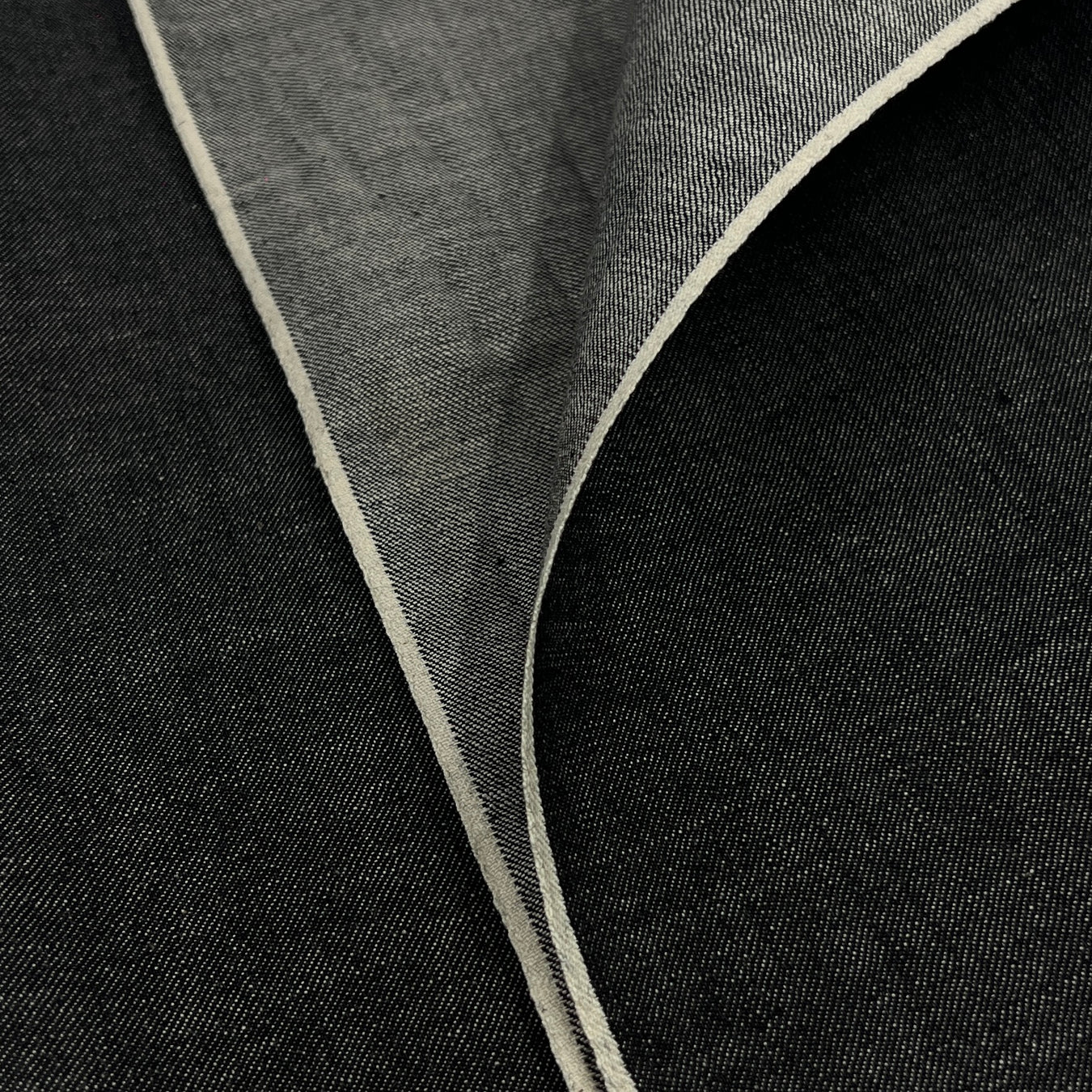 Closeup of lightweight black yarn dye selvedge denim fabric showing off both sides of selvedge. 