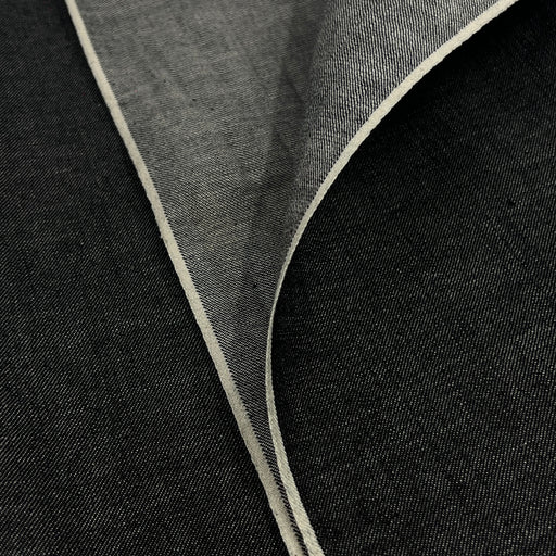 Closeup of lightweight black yarn dye selvedge denim fabric showing off both sides of selvedge. 