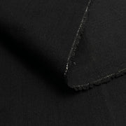 Close-up of a folded black fabric with a raw, frayed edge, showing the textile texture and weave.
