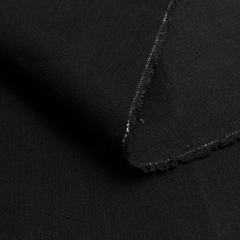 Close-up of a folded black fabric with a raw, frayed edge, showing the textile texture and weave.