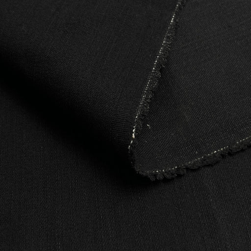 Close-up of a folded black fabric with a raw, frayed edge, showing the textile texture and weave.