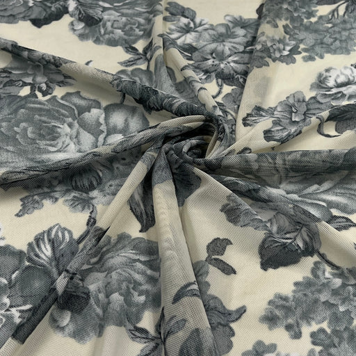 A close-up of sheer floral fabric draped in a spiral, showing a gray and black floral print on a warm cream background.