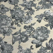 A close-up of a floral fabric with a classic toile pattern, featuring large gray and charcoal flowers and leaves on a warm cream background.