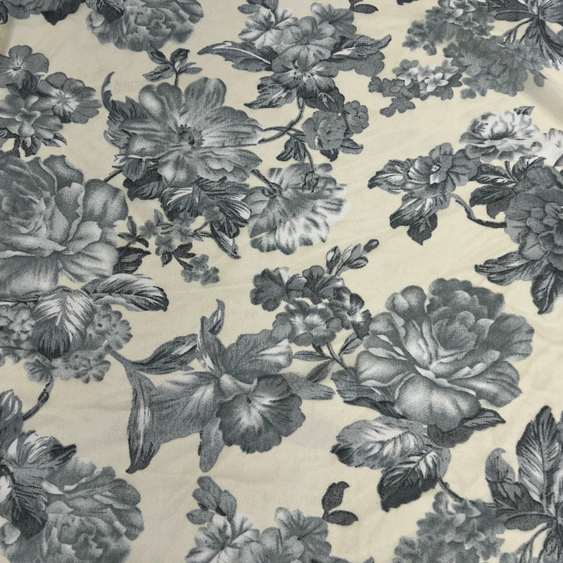 A close-up of a floral fabric with a classic toile pattern, featuring large gray and charcoal flowers and leaves on a warm cream background.