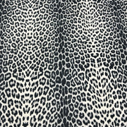 A close-up of a leopard print fabric pattern featuring black and dark gray spots on a warm off-white background.