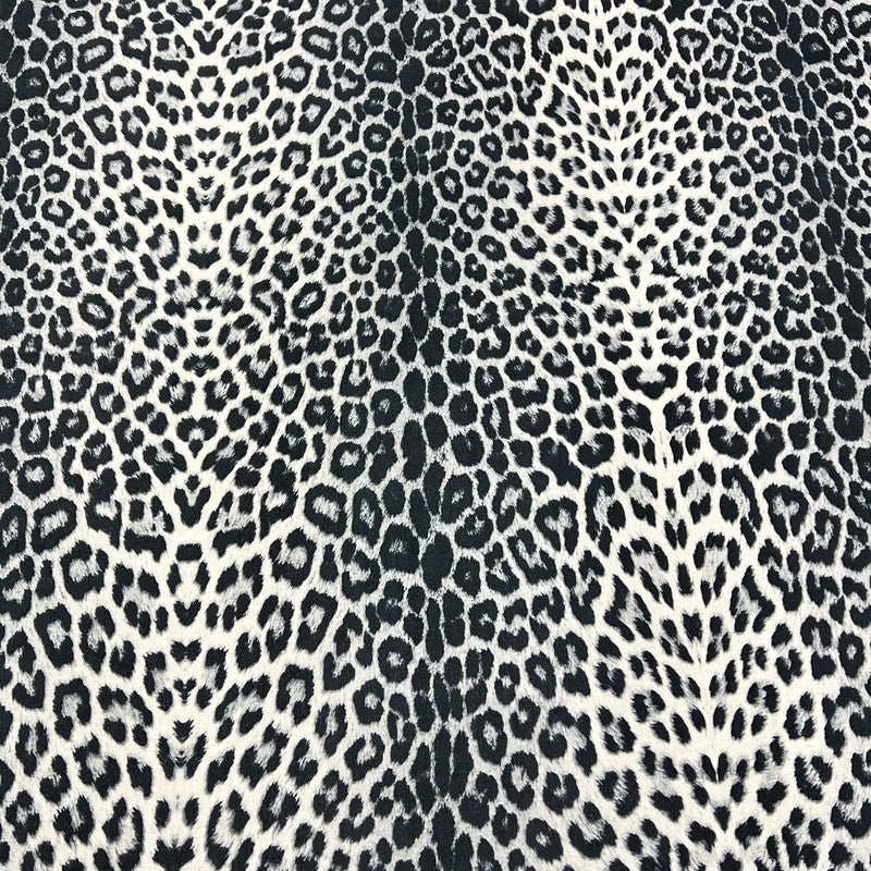 A close-up of a leopard print fabric pattern featuring black and dark gray spots on a warm off-white background.