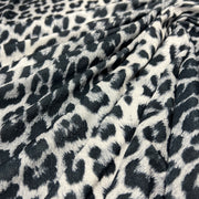 Leopard print fabric draped in soft folds, featuring a black and dark gray spotted pattern on a warm off-white background.