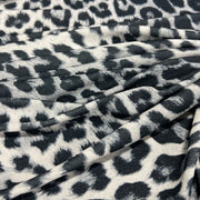 A close-up of draped fabric with a black and gray leopard print pattern on a white background.
