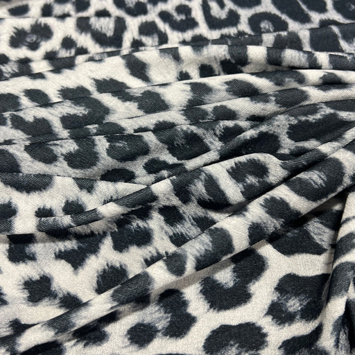 A close-up of draped fabric with a black and gray leopard print pattern on a white background.