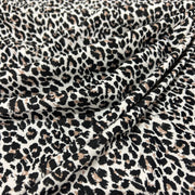 Leopard print fabric draped in soft folds, featuring a classic animal pattern with black and brown spots on a warm off-white background.