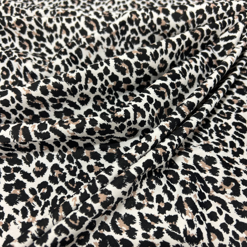 Leopard print fabric draped in soft folds, featuring a classic animal pattern with black and brown spots on a warm off-white background.