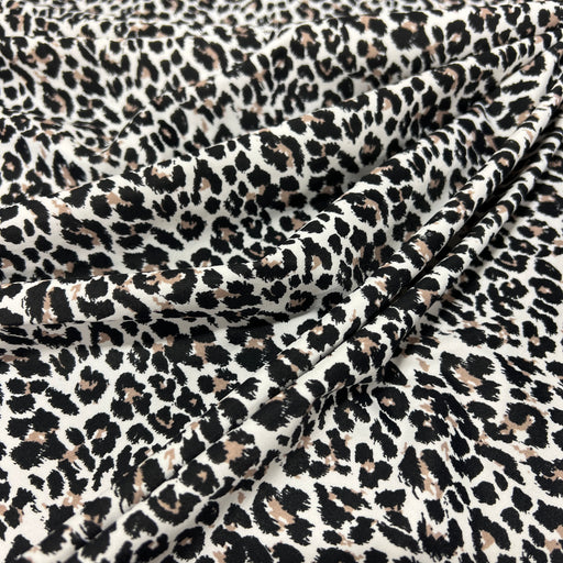Leopard print fabric draped in soft folds, featuring a classic animal pattern with black and brown spots on a warm off-white background.