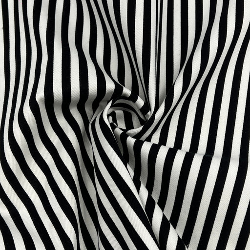 Black and white vertically striped fabric with a soft draped swirl in the center, showing a smooth woven texture.