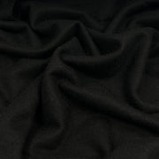 A close-up of draped black wool fabric with soft folds and a smooth matte texture.