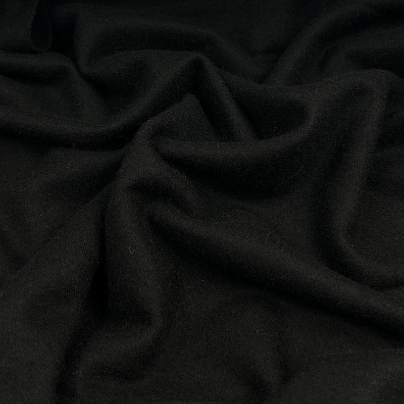 A close-up of draped black wool fabric with soft folds and a smooth matte texture.