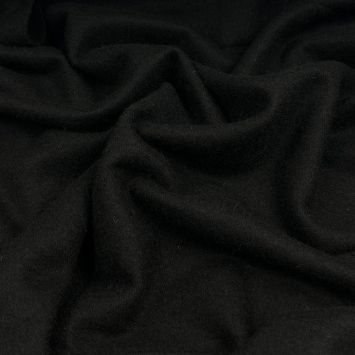 A close-up of draped black wool fabric with soft folds and a smooth matte texture.