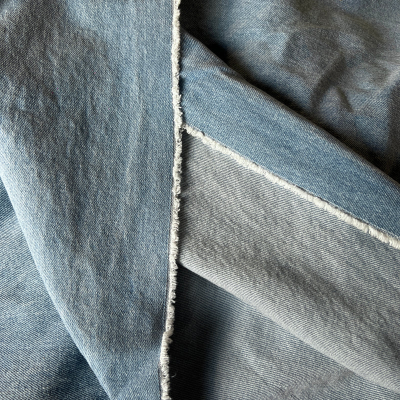 A close-up of folded light blue denim fabric showing the texture of the denim weave and a raw, frayed seam.